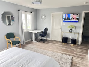 Um quarto com uma cama, uma escrivaninha, uma cadeira, uma televisão e uma porta.