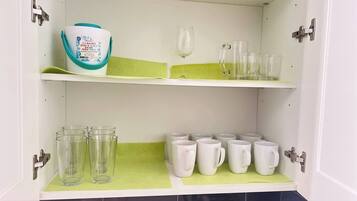A kitchen with white cabinets, a green countertop, and various glassware and mugs.