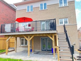 Una casa de dos pisos con un balcón, una terraza de madera y una escalera que lleva al nivel superior.