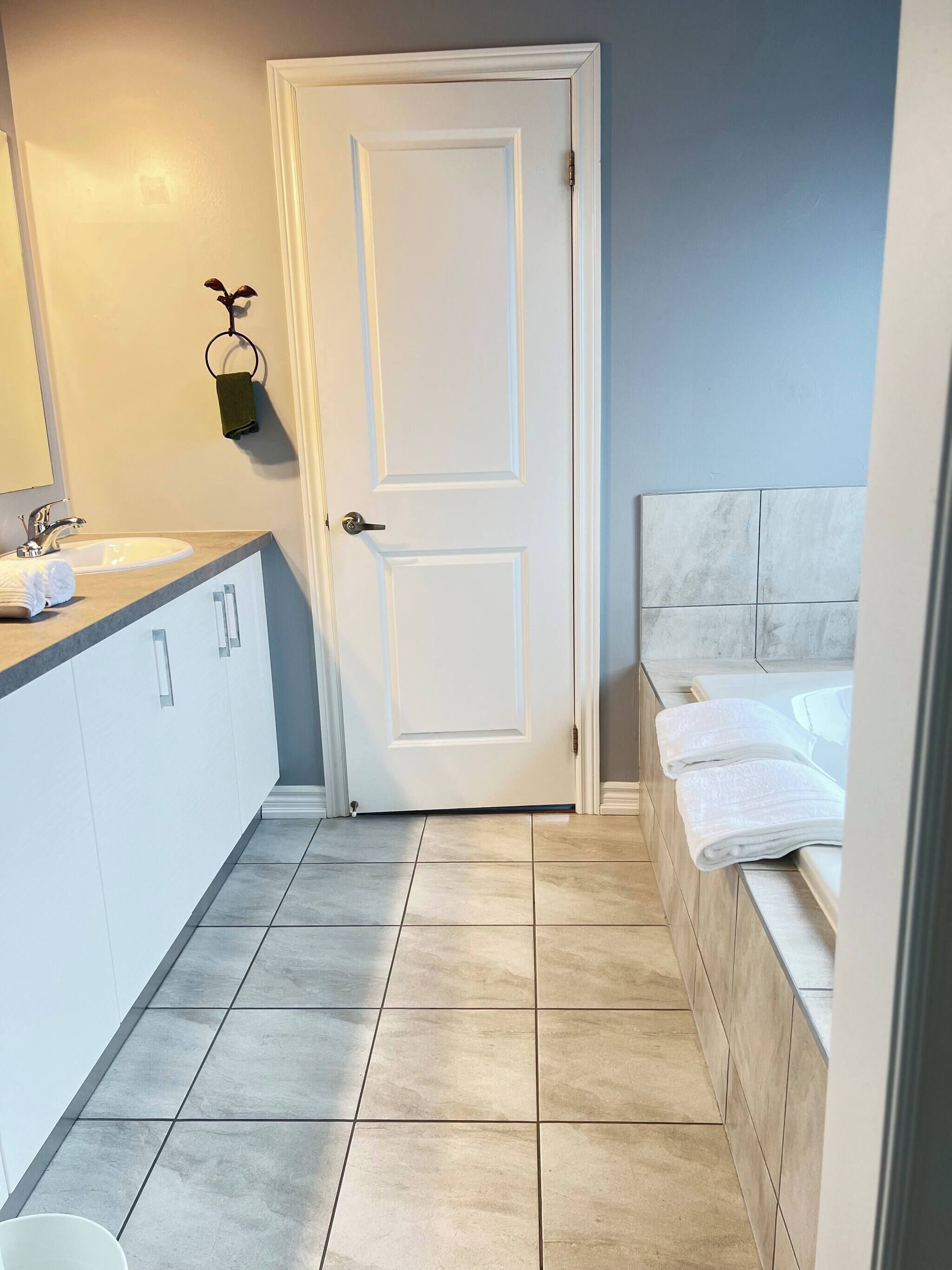 A bathroom with a white door, a sink with a mirror, and a bathtub with towels.