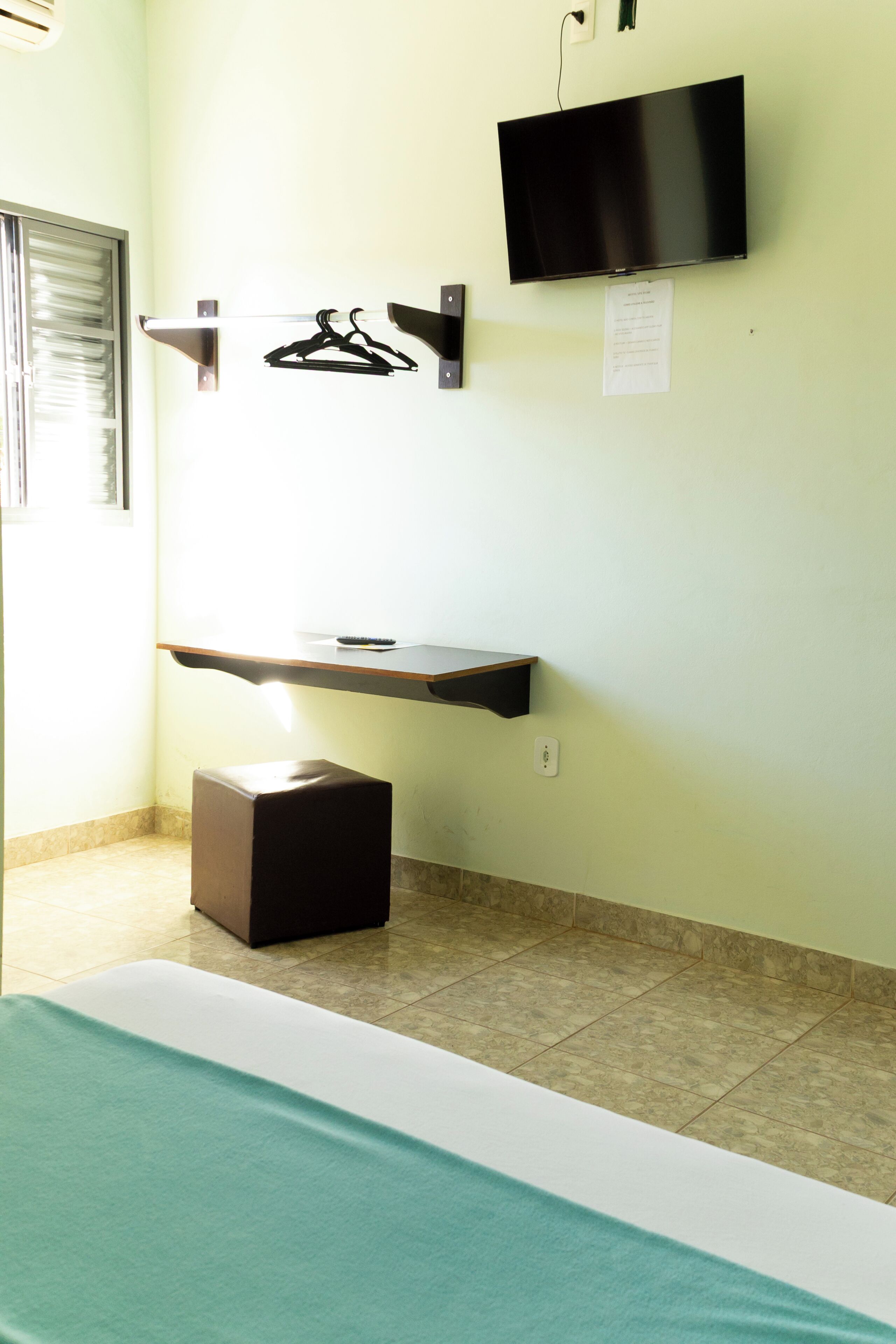 A hotel room with a bed, a TV mounted on the wall, a shelf with a remote control, and a small table.