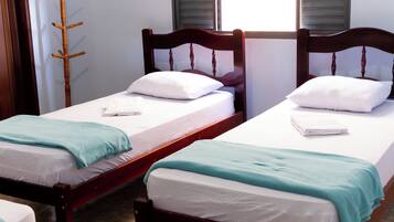 A hotel room with two single beds, each with a wooden headboard, white bedding, and a teal throw blanket.