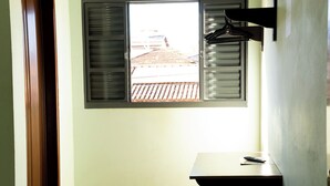 Een kamer met een raam, een flatscreen televisie aan de wand, een klein zwart voetenbankje en een betegelde vloer.
