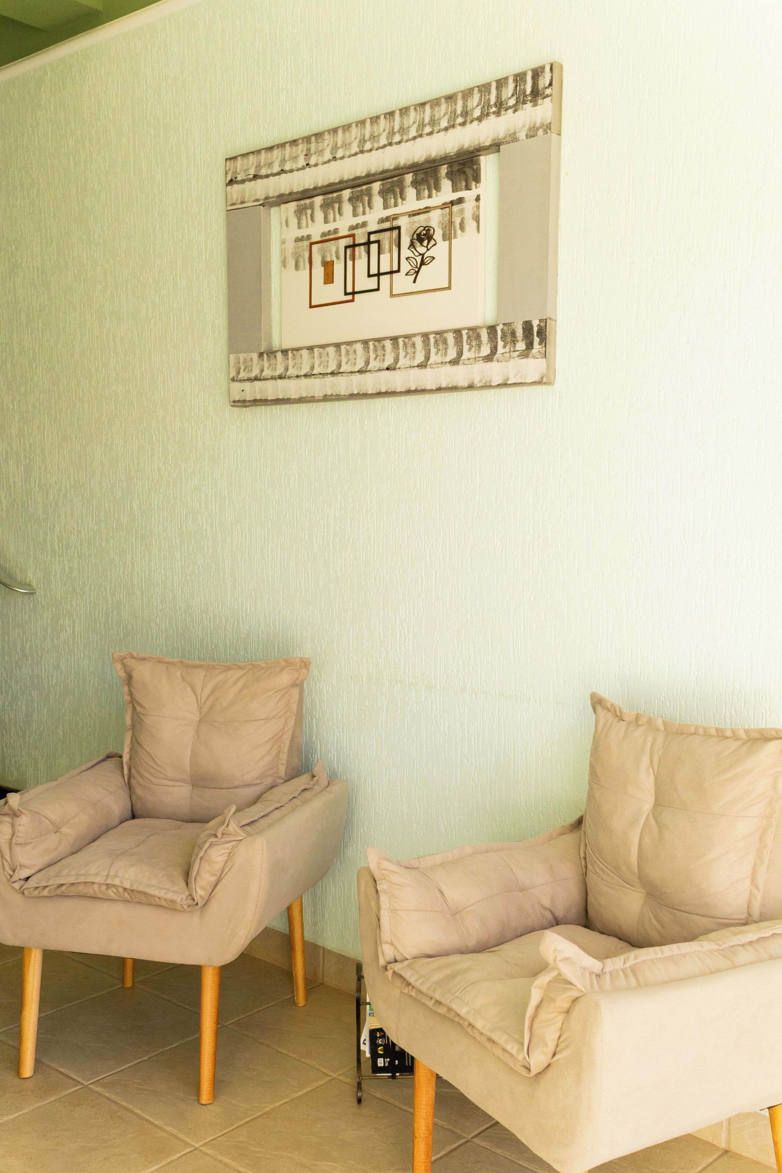 Una habitación con dos sillones color beige, un espejo en la pared y suelo de baldosas.