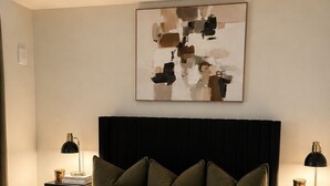 Un dormitorio con una cama, dos mesitas de noche, un cuadro abstracto en la pared y un cabecero oscuro.