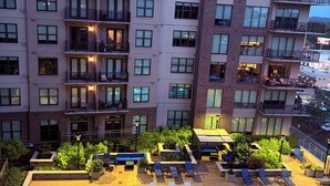 Un hotel de varios pisos con piscina en la azotea, mobiliario exterior y un jardín ajardinado.