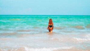Eine Strandansicht mit klarem türkisblauem Wasser und einer Person, die im Wasser steht.