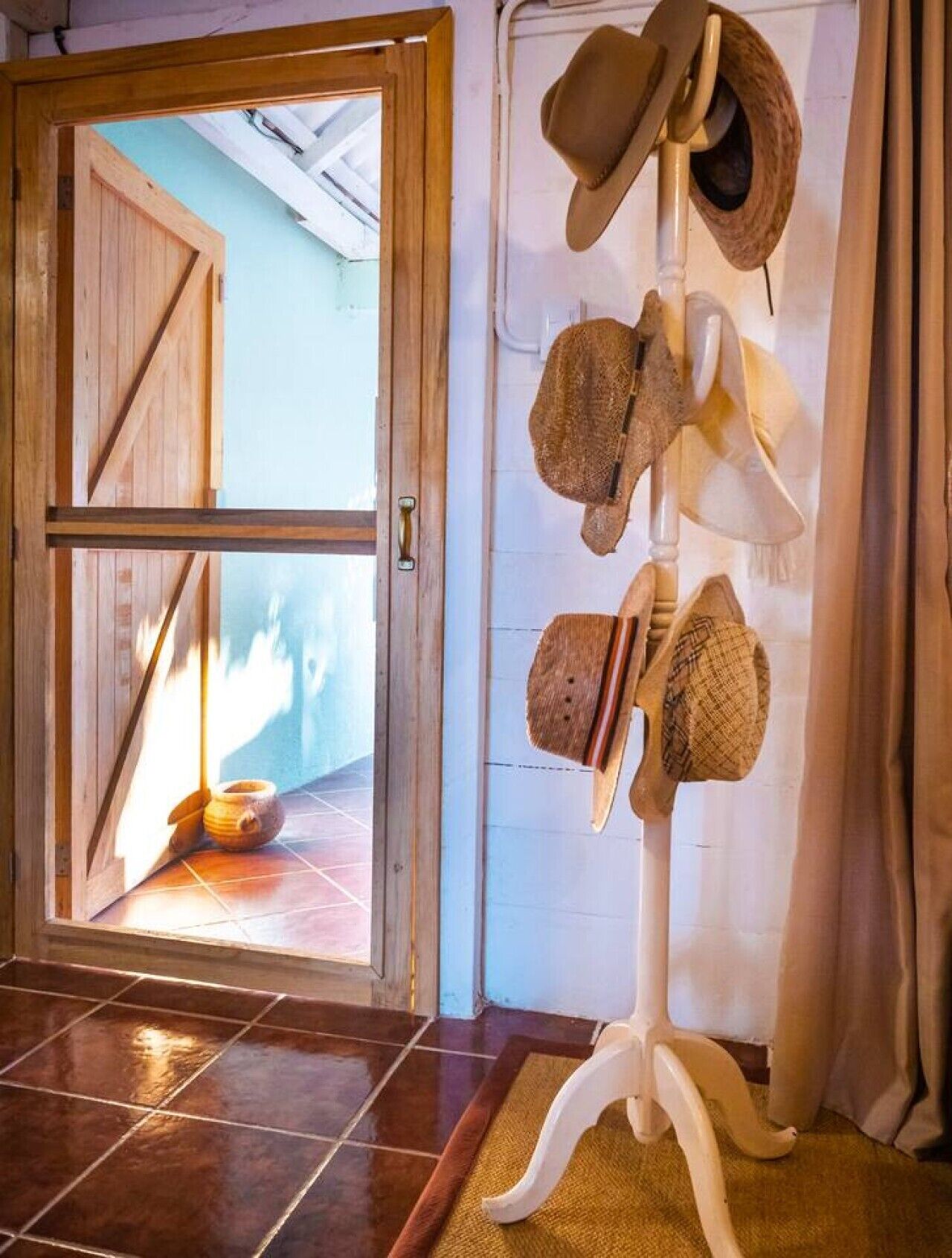 Una habitación con puerta de madera que da a un espacio con baldosas, un perchero con varios sombreros y una decoración rústica.