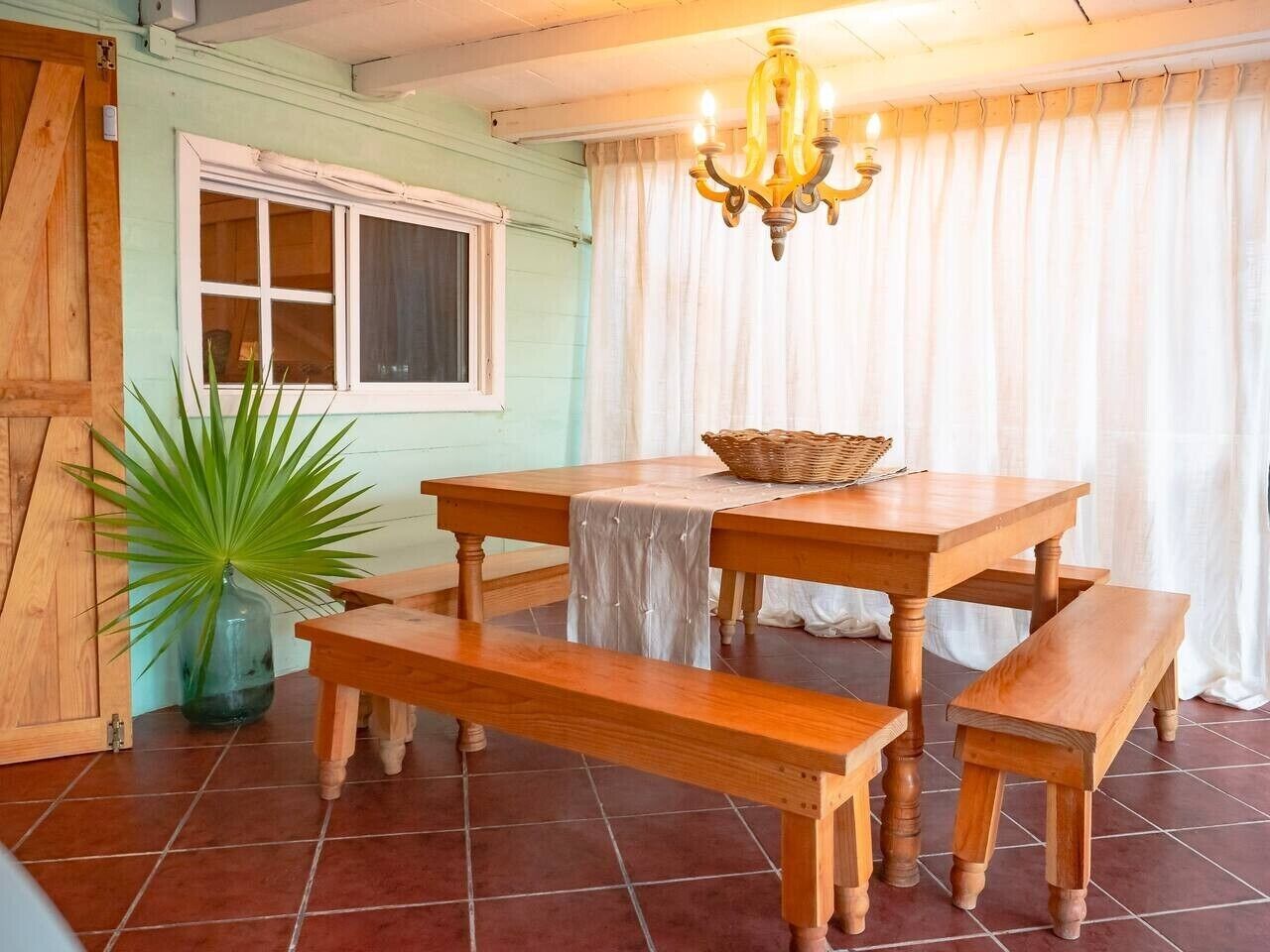 A dining area with a wooden table and benches, a chandelier, and a potted plant.