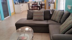 A living room with a sofa, a glass coffee table, and a kitchen in the background. - Modern Beachside Retreat • Pool•Parking•Fast Wi-Fi (Playa Agua Blanca)