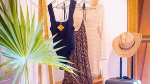 Une pièce comprenant un porte-manteau en bois, une valise, un chapeau, une plante, une petite table et une paire de sandales.