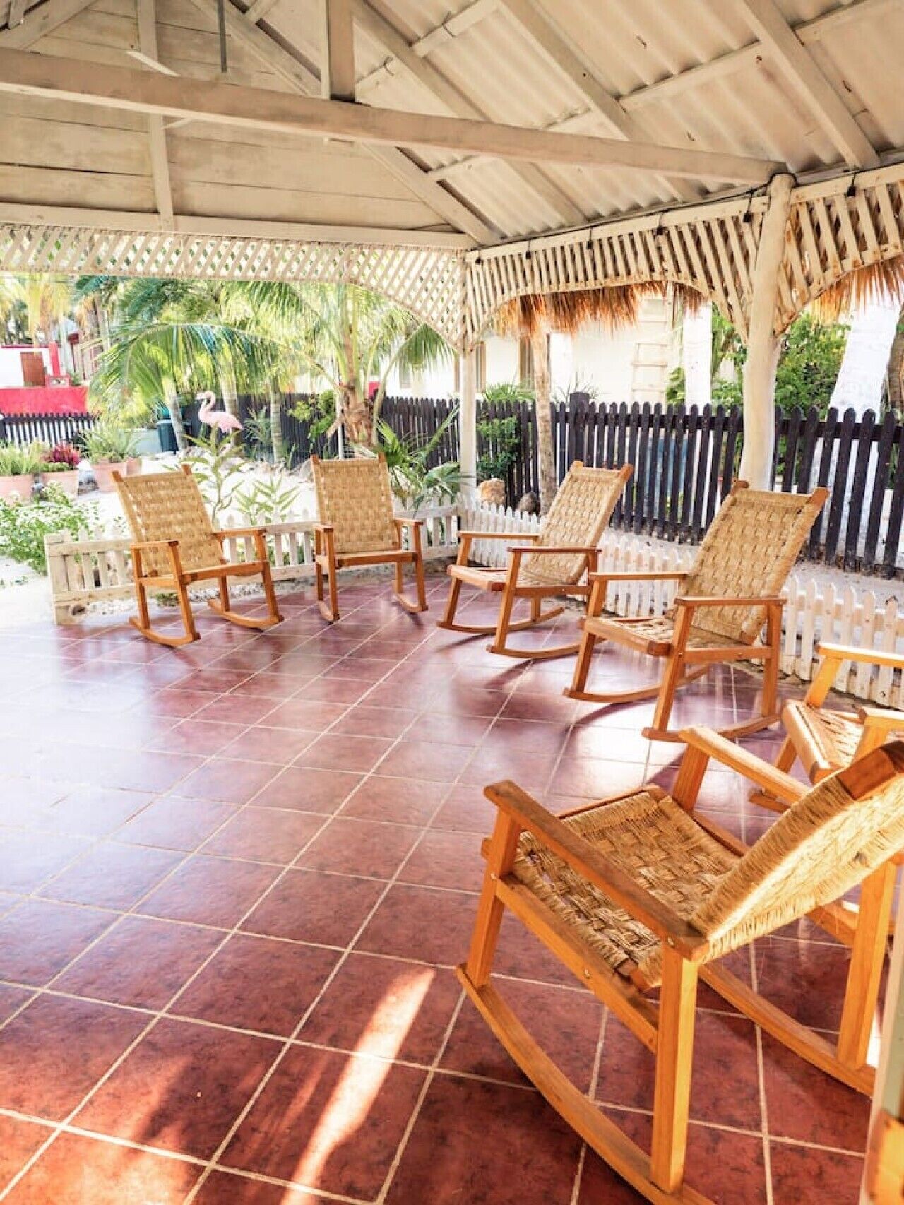 Een overdekt terras met houten stoelen en een betegelde vloer.