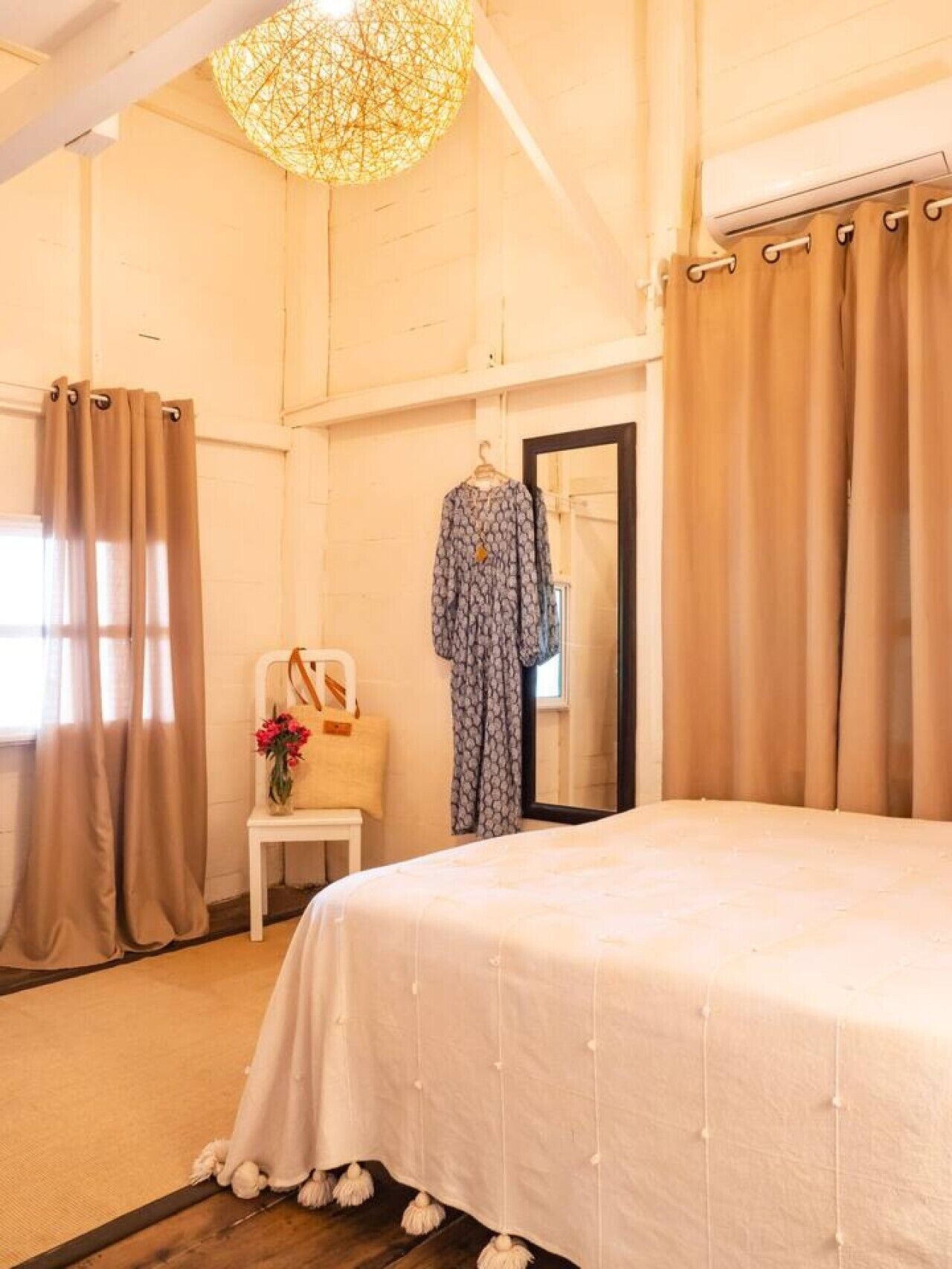 Een slaapkamer met een bed, een kapstok, een stoel met een tas en een spiegel.