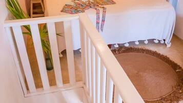 Un dormitorio con cabecera de madera, una cama con ropa blanca, una mesita de noche con un florero y una barandilla blanca.