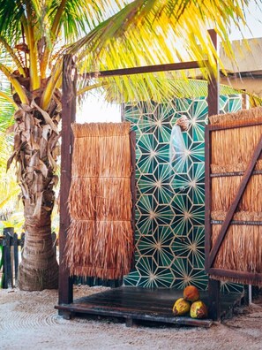 A thatched structure with a geometric patterned wall, palm trees, and a wooden bench with coconuts.