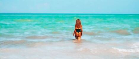A beach scene with clear turquoise water and a person standing in the water.