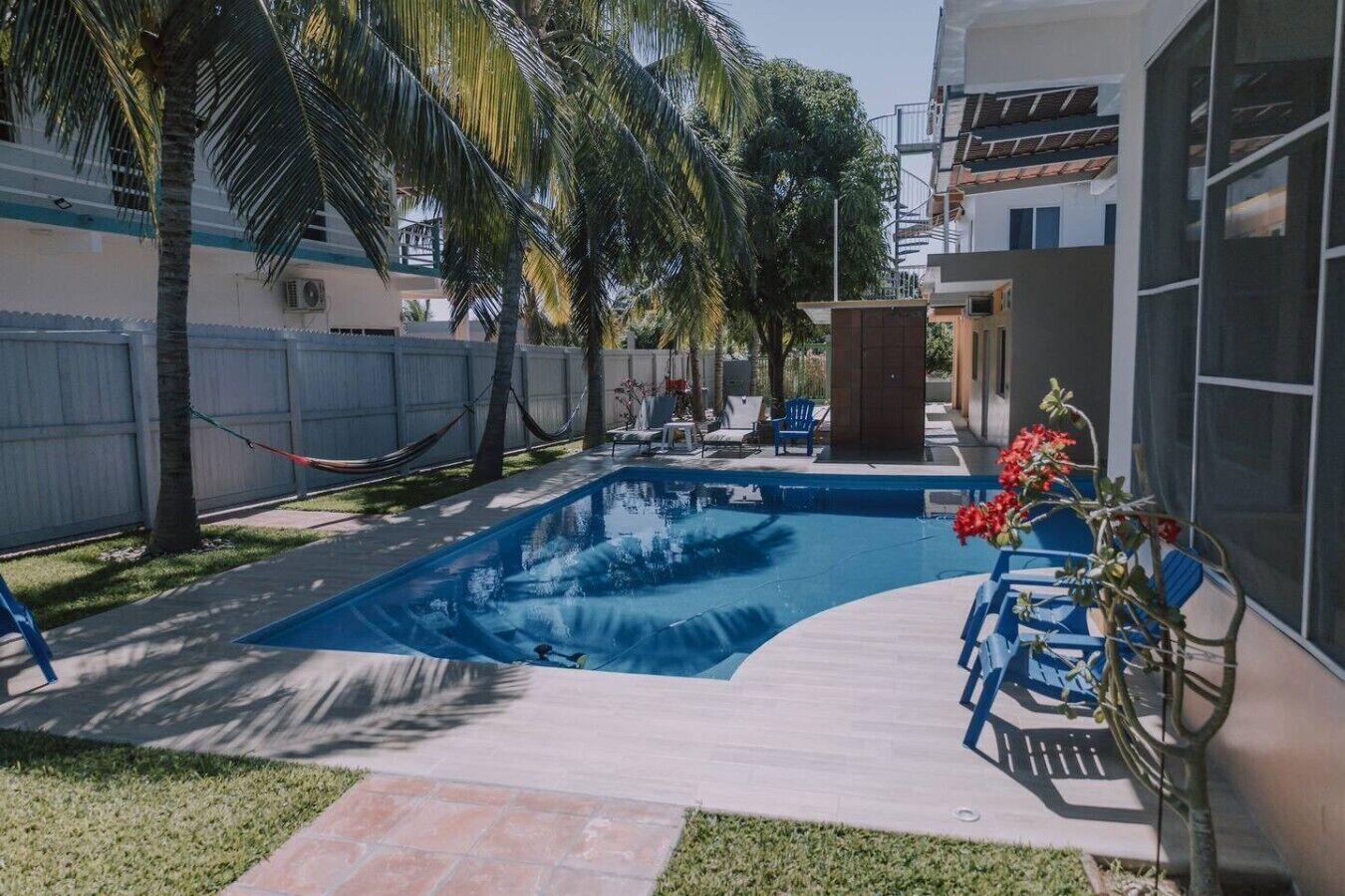 Ein Swimmingpool mit umlaufender Terrasse, Palmen und einem eingezäunten Bereich.