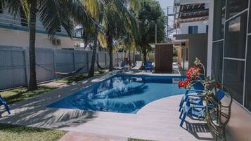 Ein Swimmingpool mit umlaufender Terrasse, Palmen und einem eingezäunten Bereich.
