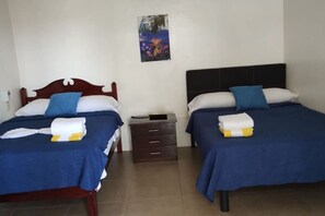Een hotelkamer met twee bedden, elk met blauw beddengoed en witte kussens. Daartussen staat een klein houten nachtkastje met een lade en een lamp. Boven de bedden hangt een schilderij.