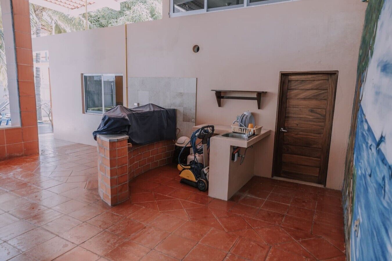 A corner room with a tiled floor, a small brick counter, a door, and a window.