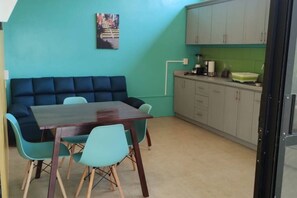 Et værelse med en teal-farvet væg, en mørkeblå sofa, et træspisebord med fire stole og et tekøkken med skabe og en bordplade.