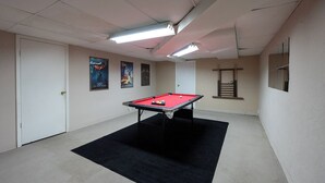 Una mesa de billar en una habitación con paredes blancas, alfombra negra y luces de techo.