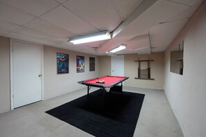 A pool table in a room with white walls, a black carpet, and ceiling lights.
