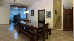 Un comedor amplio con una larga mesa de madera y bancos, una cocina al fondo y una escalera que sube a otro nivel.