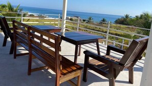 Un espacio de estar techado al aire libre con una mesa y bancos, con vistas a la costa.