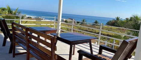 A covered outdoor seating area with a table and benches, overlooking a coastal view.