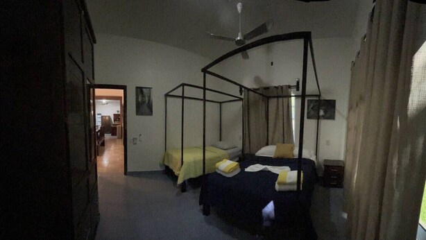 Una habitación con cama con dosel, ventilador de techo y puerta que da a otra estancia.