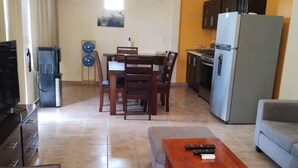 A living room with a TV, a wooden coffee table, a sofa, a dining area with a table and chairs, and a kitchen with a refrigerator. - Spacious 2BR/2.5BA Oceanview Casita with Terrace (Playa Agua Blanca)