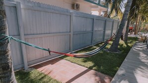A hammock tied between a wooden fence and a tree, a paved patio, and a grassy area with palm trees. - Spacious 2BR/2.5BA Oceanview Casita with Terrace (Playa Agua Blanca)