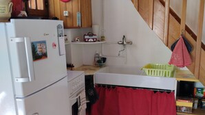 Cuina amb nevera, forn, rentamics i un cortina vermella sobre el taulell.