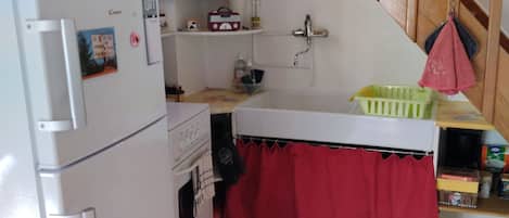 A kitchen with a refrigerator, oven, sink, and a red curtain over the counter.