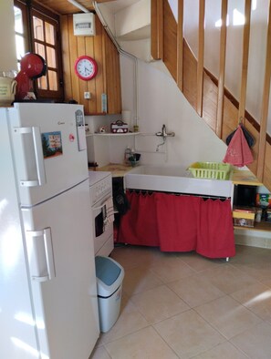 A kitchen with a refrigerator, oven, sink, and a red curtain over the counter. - A cozy little nest in the heart of the Bois Noirs (Arconsat)