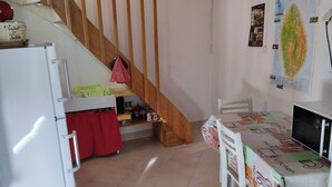 Una cuina petita amb nevera, una escala de fusta, una taula de dinar amb mantell temàtic de cuina i una paret amb un mapa.