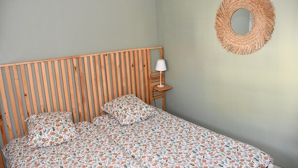 Un letto con copriletto a motivi floreali, una testiera in legno, una lampada da comodino e una decorazione murale in tessuto.