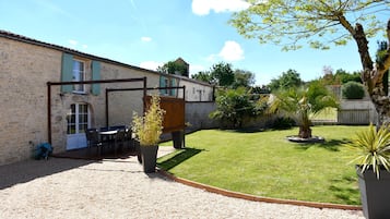 A stone building with a gravel patio, outdoor seating, and a small garden with a palm tree.