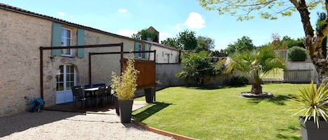 Ein Steinhaus mit Kiesterrasse, Sitzgelegenheiten im Freien und einem kleinen Garten mit einer Palme.