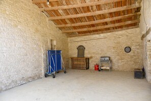 Une pièce aux murs de pierre, avec un plafond en bois, un chariot bleu, un extincteur et un jeu de fléchettes.