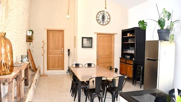 A dining area with a wooden table and chairs, a black bookshelf, a clock, and a potted plant.