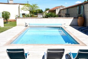 Une piscine rectangulaire à l’eau d’un bleu limpide, entourée d’une terrasse carrelée aux couleurs claires. Trois chaises longues sont alignées parallèlement à la piscine.