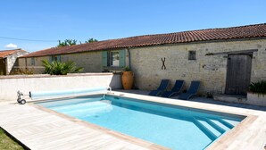 Una piscina rettangolare con un pontile in legno, un edificio in pietra con tetto in tegole e un vaso da fiori di grandi dimensioni.