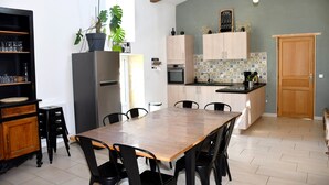Una cucina con tavolo e sedie, pensili, un frigorifero e una pianta in vaso.