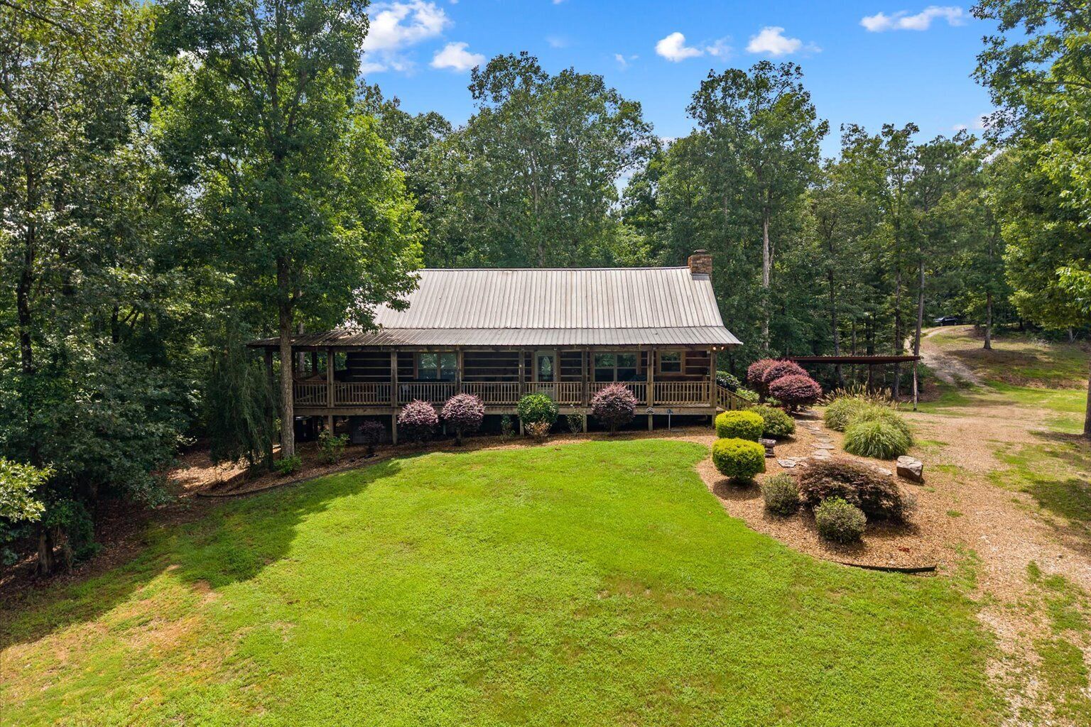 A wooden cabin with a metal roof, surrounded by a well-maintained lawn and various shrubs.