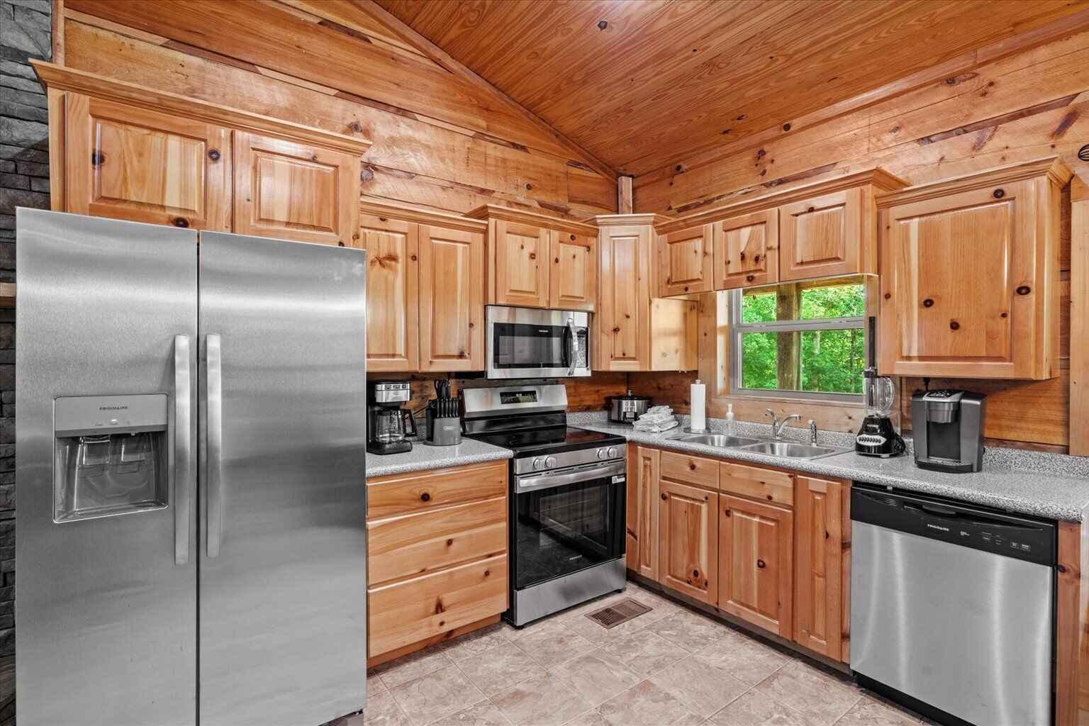 A kitchen with wooden cabinets, stainless steel appliances, and a window with a view of greenery.