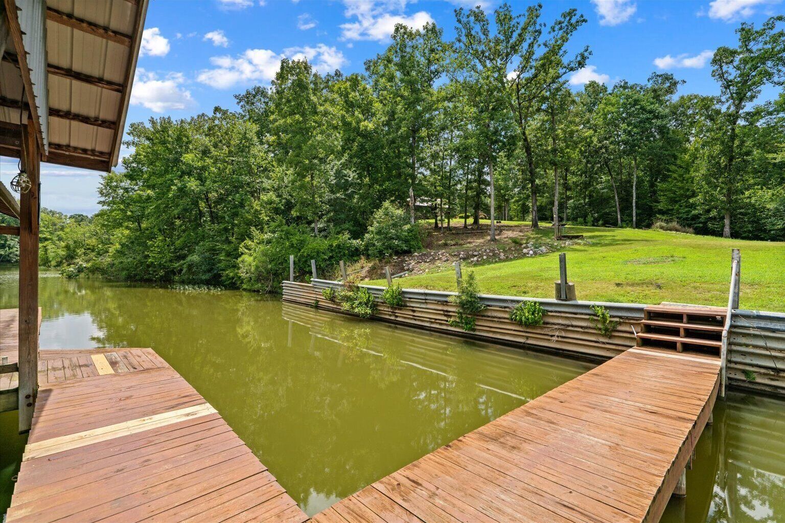 A wooden dock extending over a calm body of water, surrounded by lush greenery and trees.