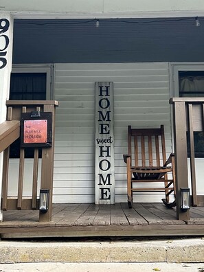 Eine Holzveranda mit einem Schild, auf dem 'HOME sweet HOME' steht, und einem Stuhl.