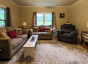 A living room with a sofa, armchair, coffee table, and a rug. - 3-bedroom farmhouse in charming Del Rio with with trout stream and 35 acres. (Del Rio)